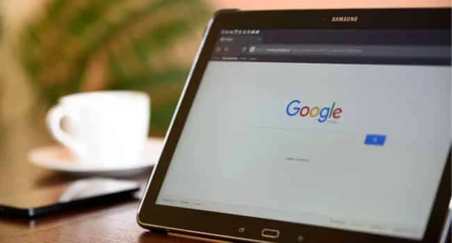 site do google sendo exibido em uma pequena tela e ao fundo uma xícara de café